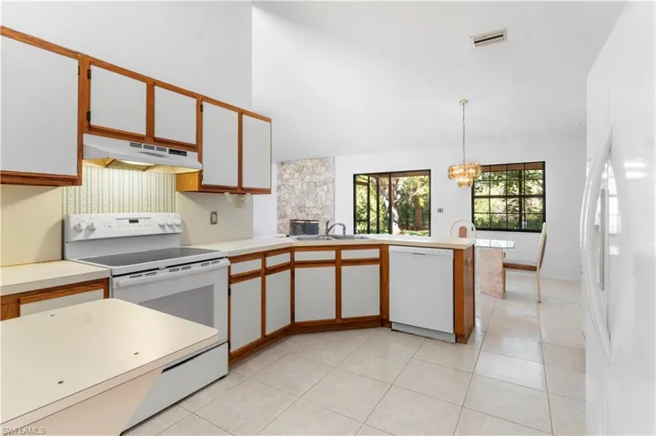 Kitchen featuring brown cabinets, light countertops, white appliances, and decorative light fixtures