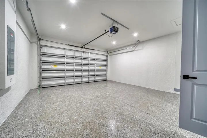 Garage with a garage door opener, electric panel, and a textured wall
