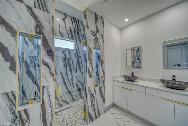 Full bath with marble finish floor, a sink, a marble finish shower, and double vanity