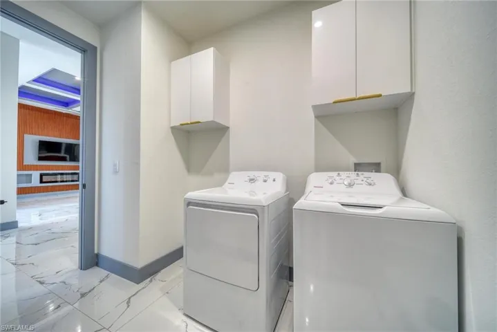 Laundry area featuring marble finish floor, washer and clothes dryer, cabinet space, and baseboards