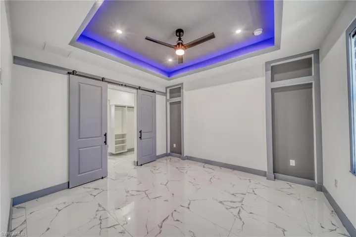 Unfurnished bedroom with a tray ceiling, baseboards, and a barn door