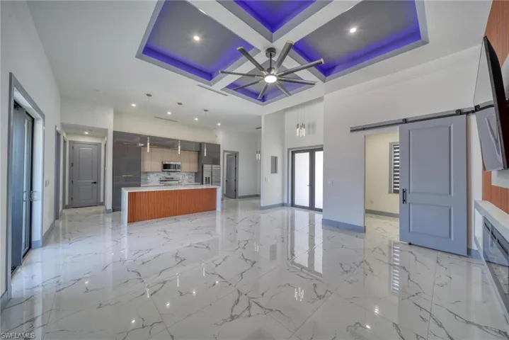 Kitchen featuring a barn door, coffered ceiling, a ceiling fan, stainless steel microwave, and open floor plan
