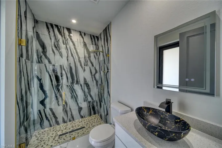 Full bath with a marble finish shower, vanity, and toilet