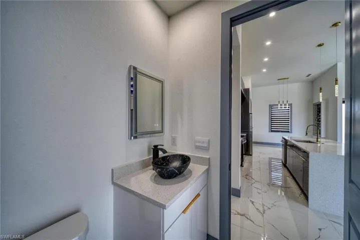 Bathroom featuring toilet, marble finish floor, two vanities, and a sink