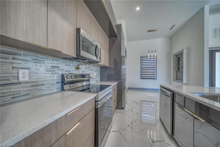 Kitchen featuring light stone counters, marble finish floor, stainless steel appliances, light brown cabinets, and modern cabinets