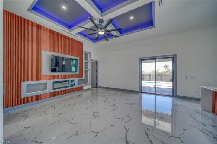 Unfurnished living room featuring marble finish floor, a ceiling fan, an accent wall, coffered ceiling, and baseboards