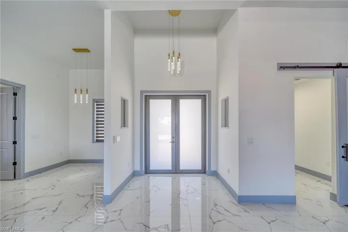 Foyer entrance with marble finish floor, french doors, a towering ceiling, a barn door, and baseboards