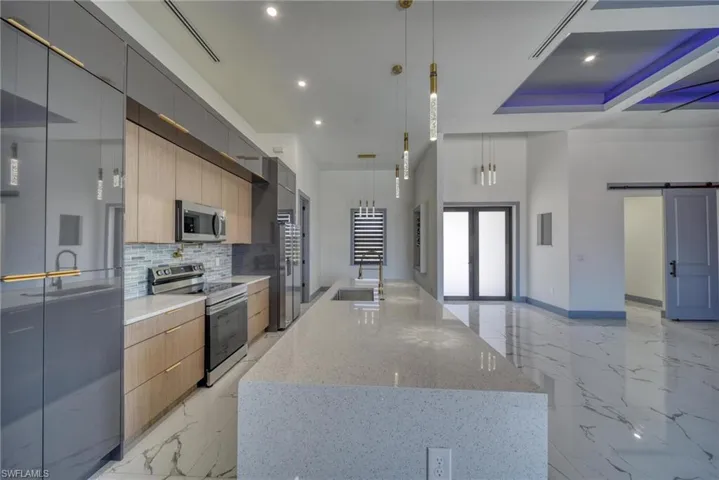 Kitchen with a barn door, a center island with sink, modern cabinets, appliances with stainless steel finishes, and marble finish floor