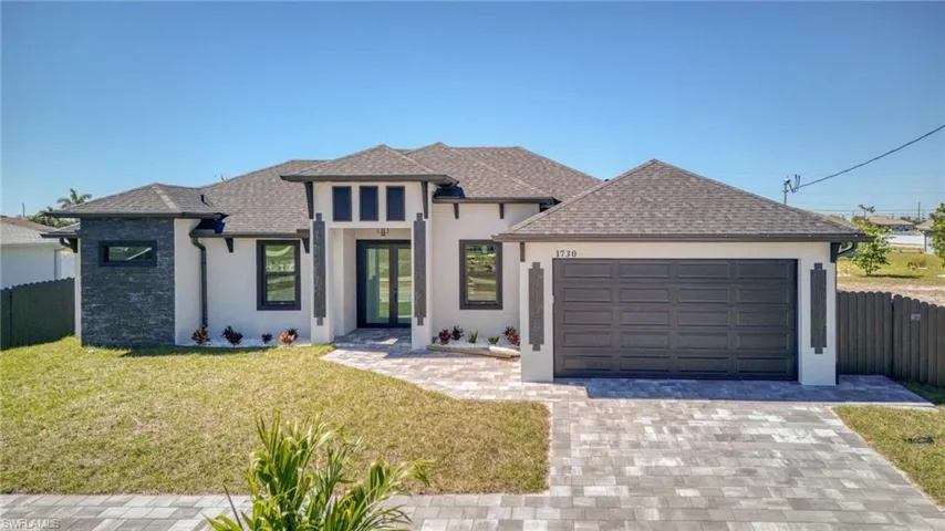 View of front of home with an attached garage, fence, decorative driveway, stucco siding, and a front yard