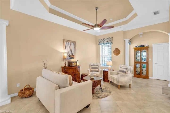 Living room with decorative columns, a raised ceiling, ornamental molding, light tile patterned floors, and a ceiling fan