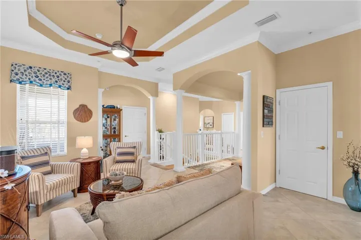Living area featuring light tile patterned floors, decorative columns, crown molding, arched walkways, and ceiling fan