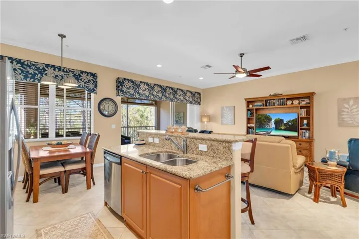 Kitchen featuring light stone countertops, a center island with sink, open floor plan, recessed lighting, and decorative light fixtures