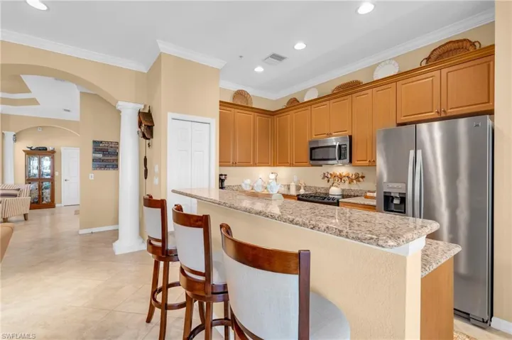 Kitchen featuring arched walkways, appliances with stainless steel finishes, ornamental molding, light stone countertops, and a kitchen island