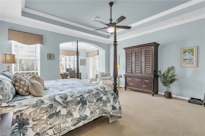 Carpeted bedroom featuring a raised ceiling, ornamental molding, and a ceiling fan