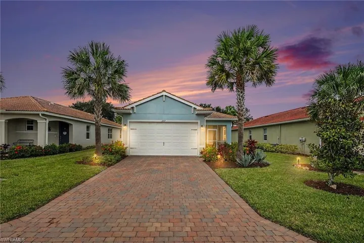 Paver driveway with integrated landscape lighting, manicured lawn, and mature palm trees