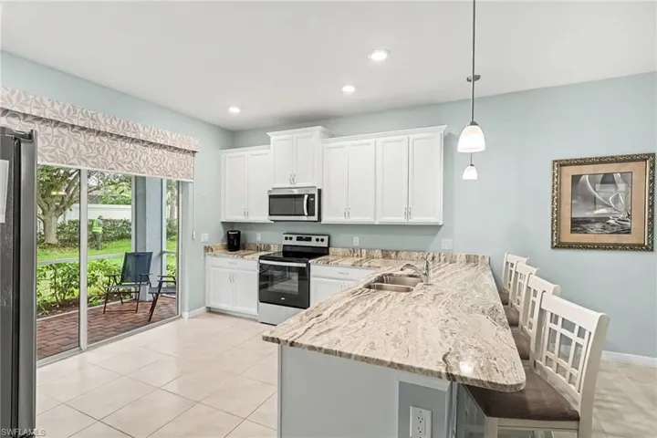 White cabinetry, stainless steel appliances, light-toned countertop, tile flooring, and sliding glass doors to a brick patio