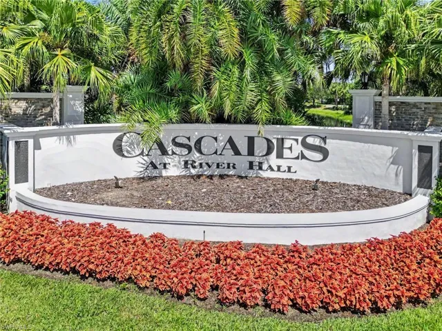 Community entrance sign featuring a stucco finish, stacked stone accents, and mature tropical landscaping