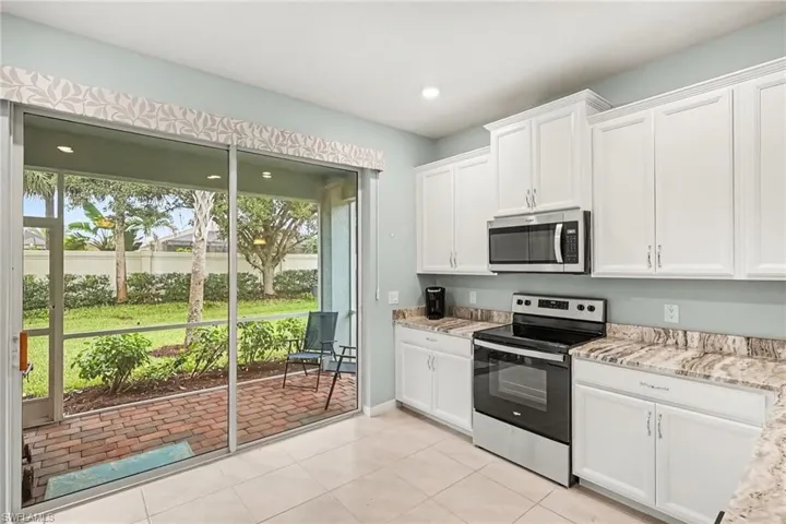 White cabinetry, stainless steel appliances, neutral tile flooring, and a screened patio with brick pavers