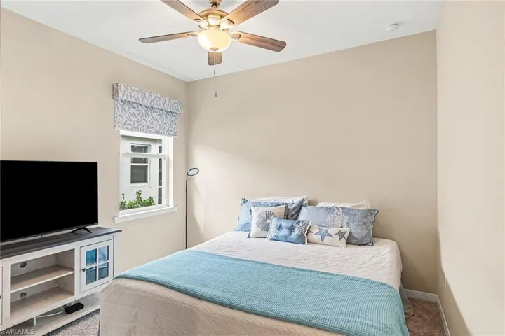 Window with a patterned Roman shade, ceiling fan with integrated lighting, and neutral wall paint