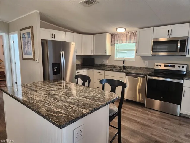 Kitchen with white cabinets, stainless steel appliances, wood-type flooring, and a center island