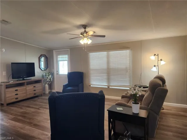 Living room featuring ceiling fan, crown molding, and dark wood-type flooring