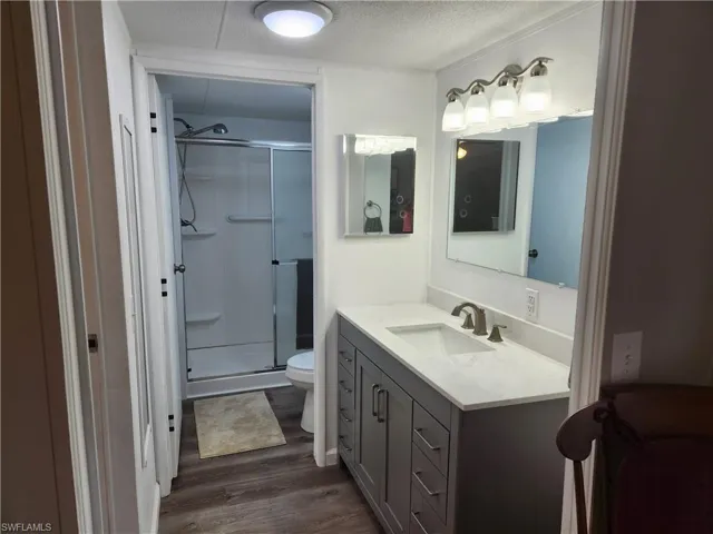 Bathroom featuring hardwood / wood-style floors, an enclosed shower, a textured ceiling, toilet, and vanity