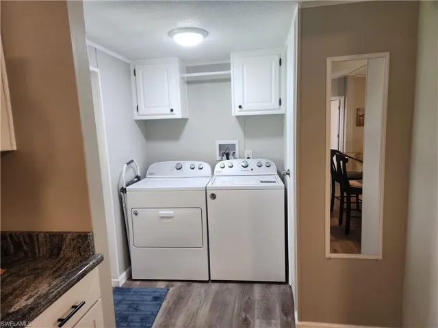 Washroom featuring wood-type flooring, washer and clothes dryer, cabinets, and a textured ceiling