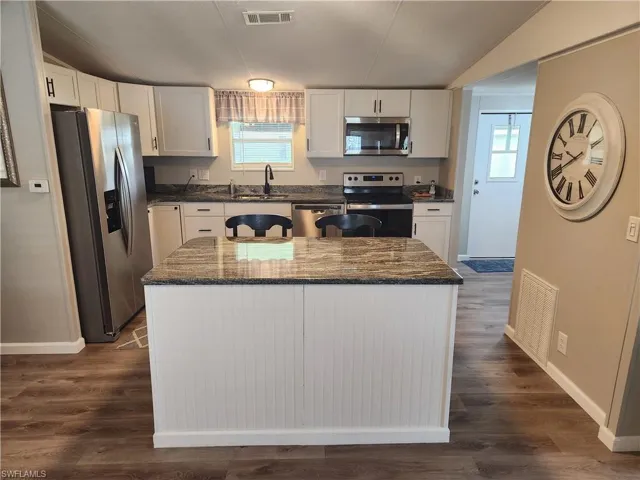 Kitchen featuring white cabinetry, stainless steel appliances, a kitchen island, and dark wood-type flooring
