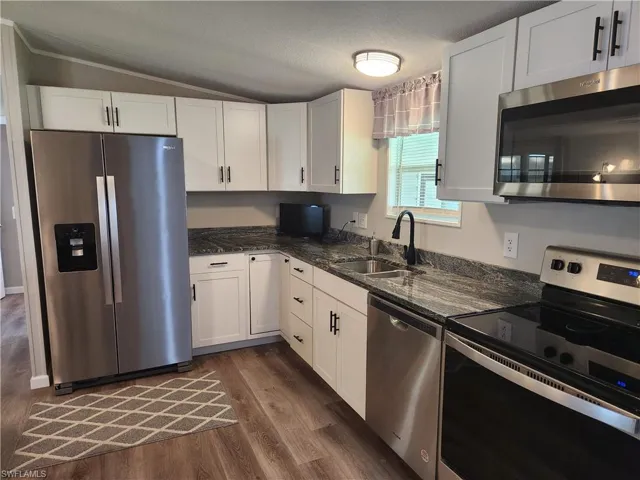 Kitchen with sink, appliances with stainless steel finishes, dark wood-type flooring, and white cabinetry