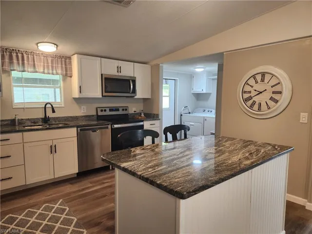 Kitchen featuring stainless steel appliances, sink, white cabinetry, a center island, and dark wood-type flooring