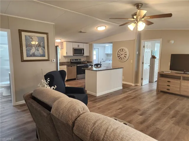 Living room with washer / clothes dryer, ceiling fan, dark hardwood / wood-style flooring, and vaulted ceiling