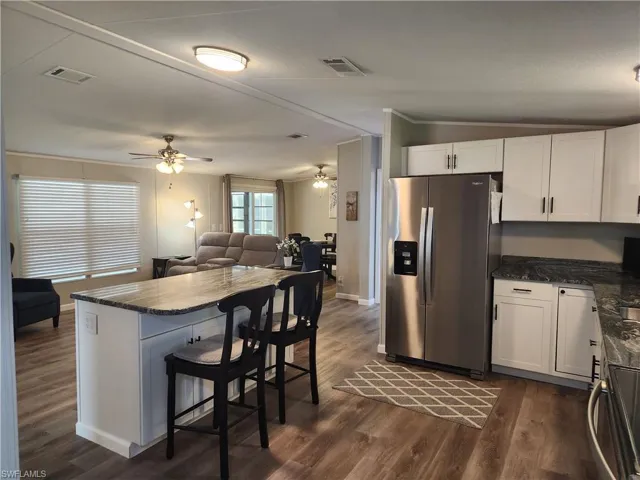 Kitchen with stainless steel fridge, white cabinets, ceiling fan, and dark hardwood / wood-style floors