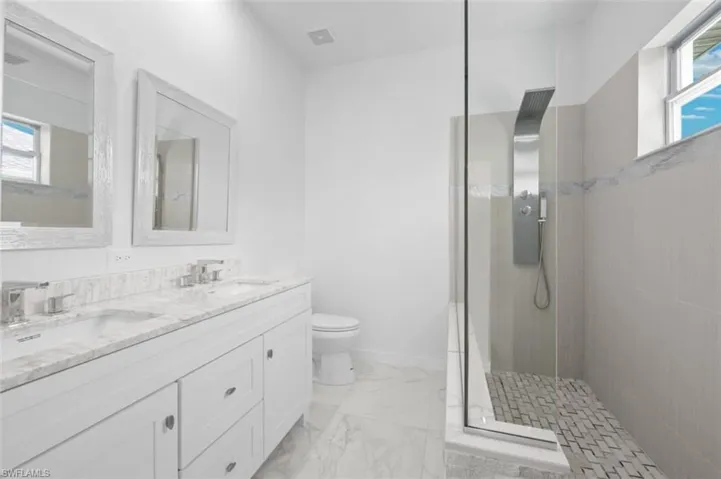 Bathroom featuring tile floors, dual sinks, a healthy amount of sunlight, and a tile shower