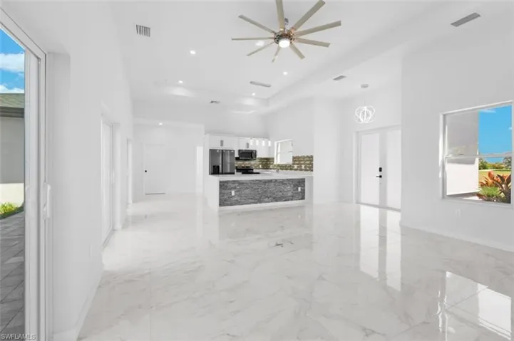 Kitchen with a tray ceiling, light tile flooring, backsplash, white cabinets, and appliances with stainless steel finishes