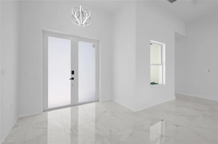 Spare room with an inviting chandelier, light tile flooring, and french doors