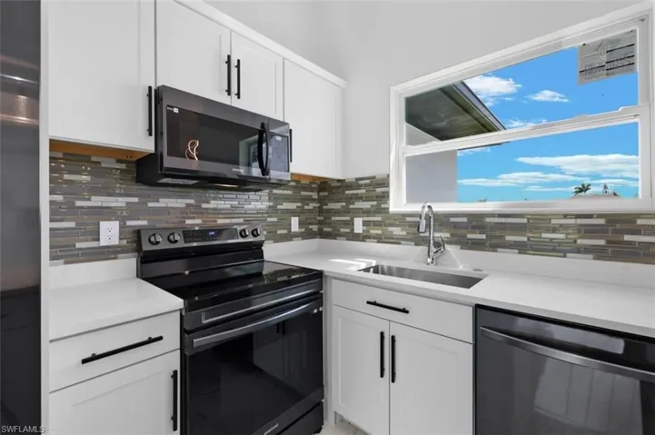 Kitchen featuring sink, backsplash, white cabinetry, and appliances with stainless steel finishes
