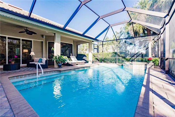 Screened outdoor pool area featuring a built-in spa, paver decking, and a covered lanai with a ceiling fan