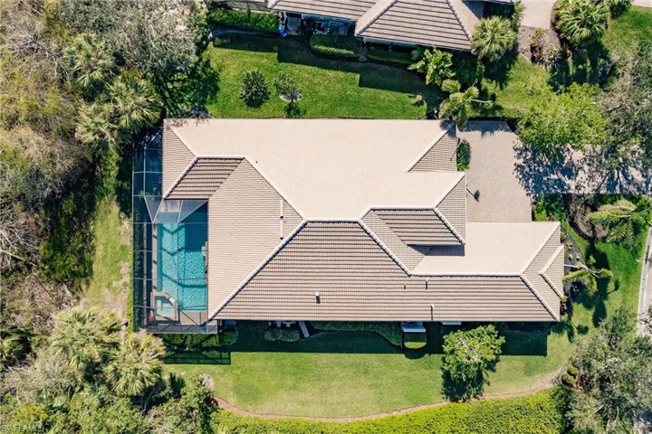 Terracotta tile roof, screened swimming pool, manicured lawn, paved driveway, and mature landscaping
