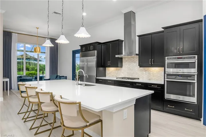 Kitchen featuring appliances with stainless steel finishes, wall chimney exhaust hood, a center island with sink, pendant lighting, and a breakfast bar area