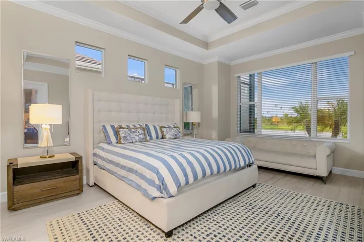 Bedroom featuring ceiling fan, a raised ceiling, light hardwood / wood-style floors, and ornamental molding
