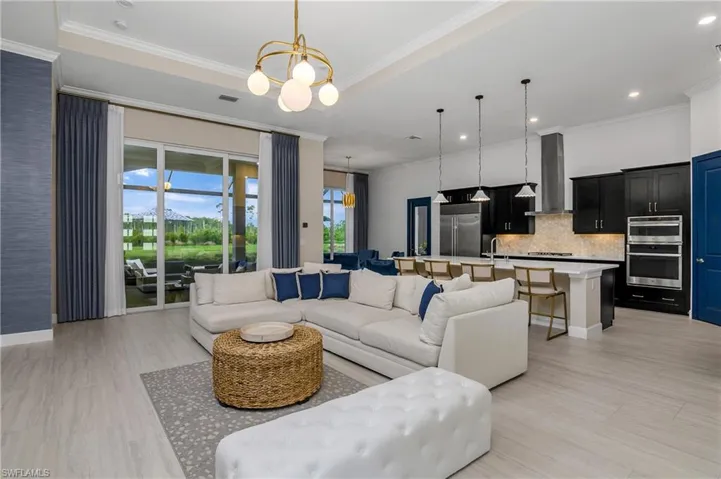 Living room with a tray ceiling, a notable chandelier, ornamental molding, and sink