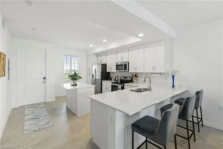 Kitchen with a kitchen breakfast bar, a center island, appliances with stainless steel finishes, a peninsula, and white cabinetry