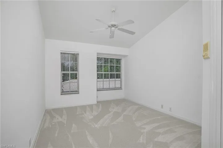 Carpeted empty room featuring vaulted ceiling, a ceiling fan, and baseboards