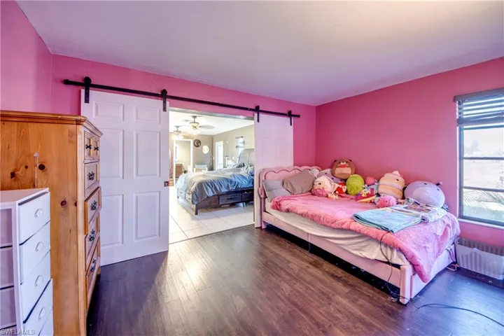 Bedroom with a barn door, dark wood-style floors, and radiator