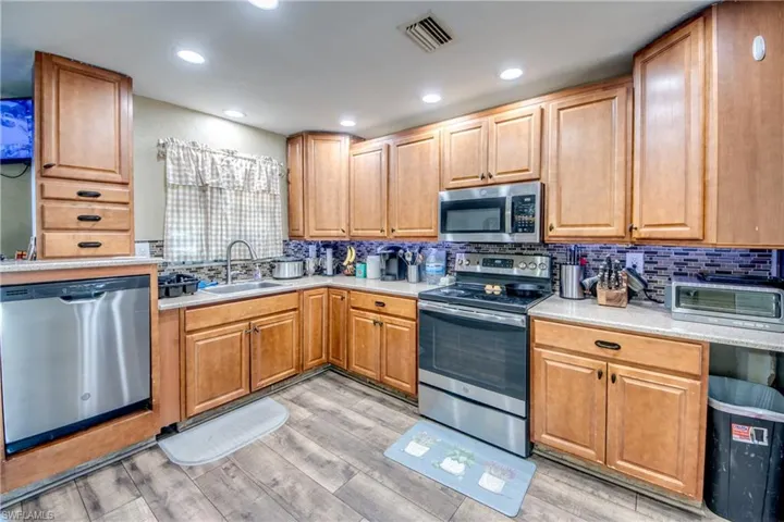 Kitchen with stainless steel appliances, tasteful backsplash, light wood-type flooring, recessed lighting, and light stone counters