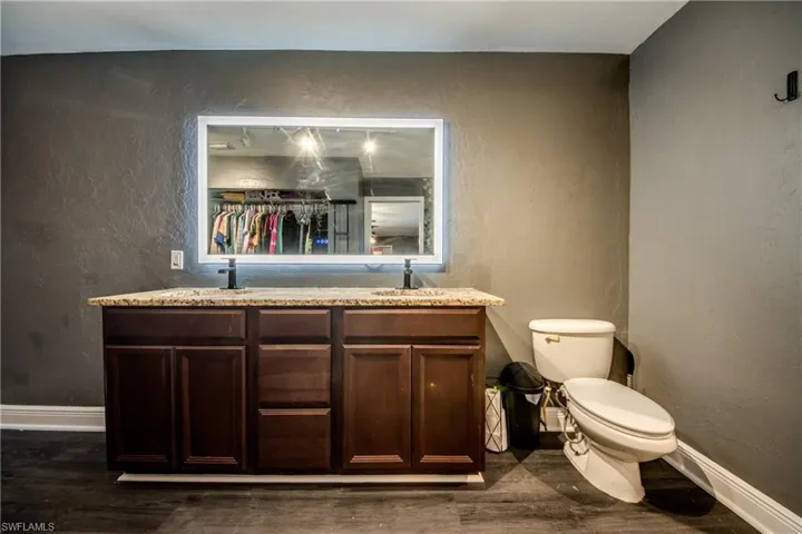 Full bath featuring a textured wall, double vanity, and dark wood-type flooring