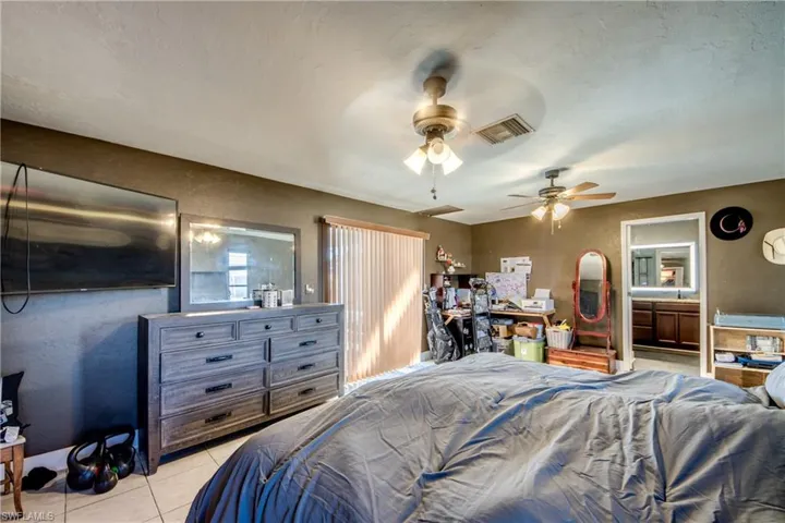 Bedroom with ceiling fan, light tile patterned flooring, and a textured wall