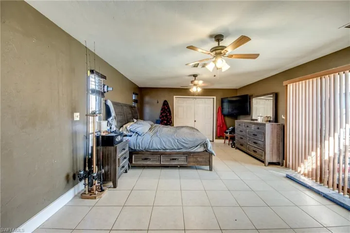 Bedroom with a closet, a ceiling fan, light tile patterned floors, and a textured wall
