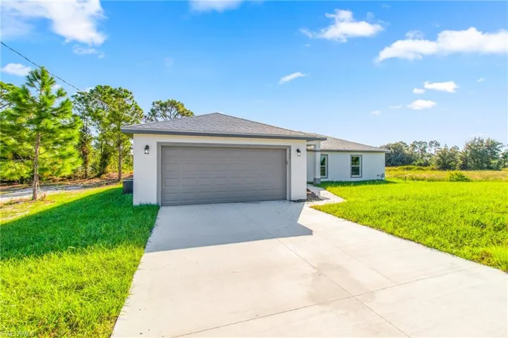 Ranch-style home featuring a front yard, stucco siding, driveway, and an attached garage