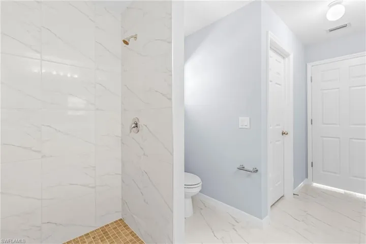 Bathroom with light marble finish flooring and a marble finish shower